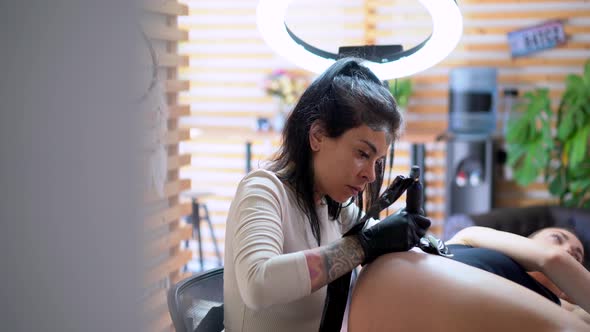 Tattooer drawing tattoo on hip of client in studio alt