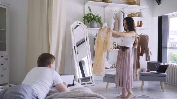 Woman Shows Dress To Boyfriend Working with Laptop on Bed