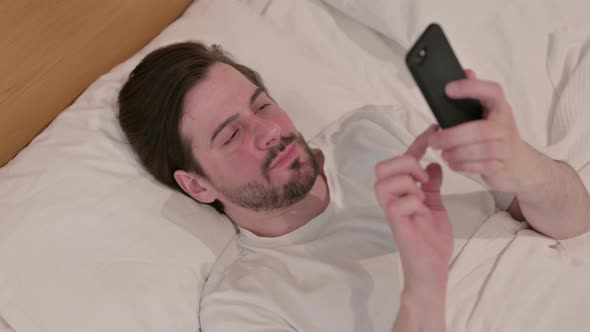 Casual Young Man Using Smartphone While Sleeping in Bed alt