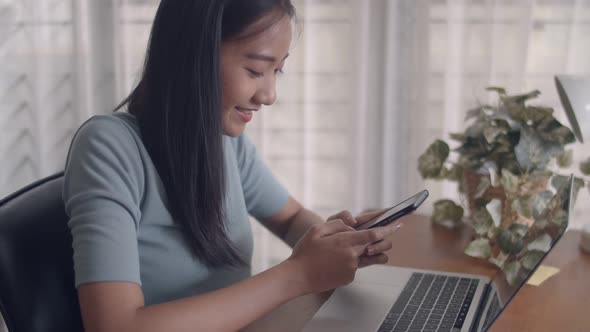 Asian woman smiling hands typing mobile phone and scrolls through social media feeds.