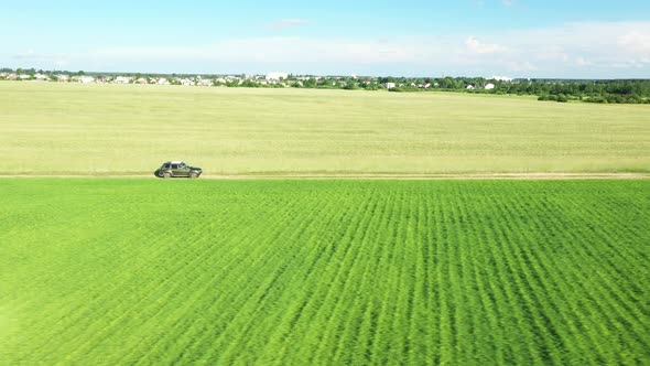 Aerial View Of Car SUV In Motion Moving On Countryside Road Through Summer Green Fields