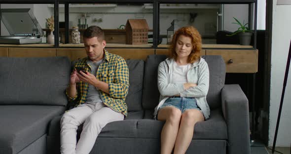 Man Is Sitting on Sofa, Using Smartphone, Woman Is Irritated By Man alt