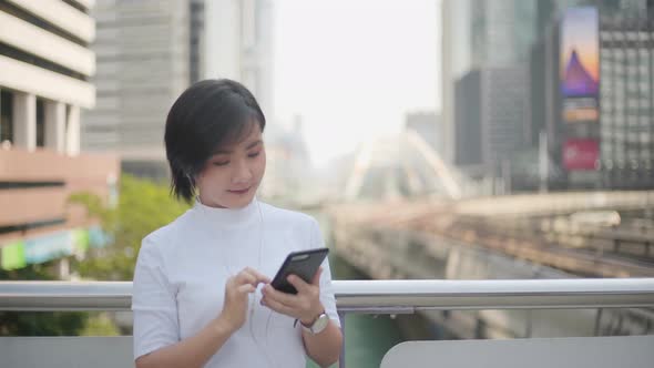 Portrait of asian woman with earphone listening music and using smartphone for chatting