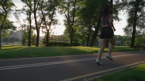 SLOW MOTION CLOSE UP Female Running in Green Park in Small Suburban Town with Tall Buildings in the