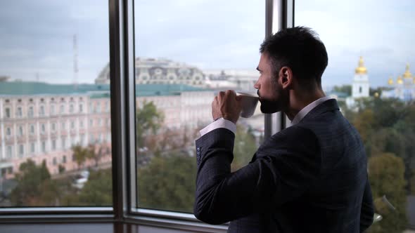 Businessman Drinking Coffee Standing By Window alt