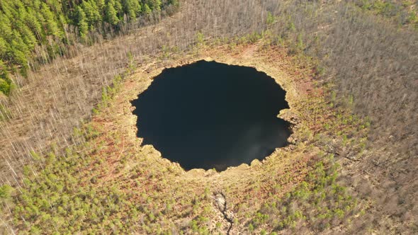 AERIAL: Rotating Shot of Round Deep Blue Lake in Forest on Sunny Day
