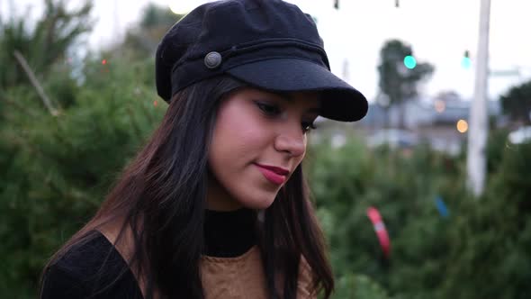 A young woman shopping on a Christmas tree lot with green douglas fir conifers in a holiday botanica alt