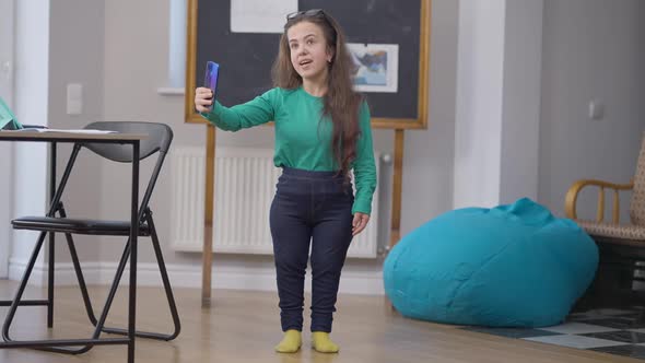 Wide Shot Positive Confident Blogger Standing Indoors Talking at Smartphone Waving Saying Goodbye to alt