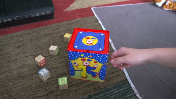 A woman's hand winding a jack-in-the-box toy until it pops up. Shot in slow motion alt