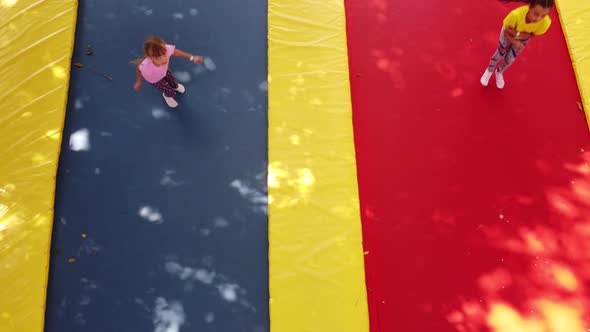 Two Little Girls in the Summer Jump on a Trampoline Smiling and Laughing