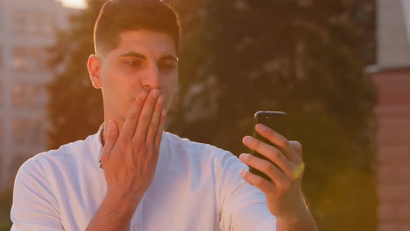 Smiling Millennial Indian Arabic Male Student Holding Phone Making Video Call Talking to Parents alt
