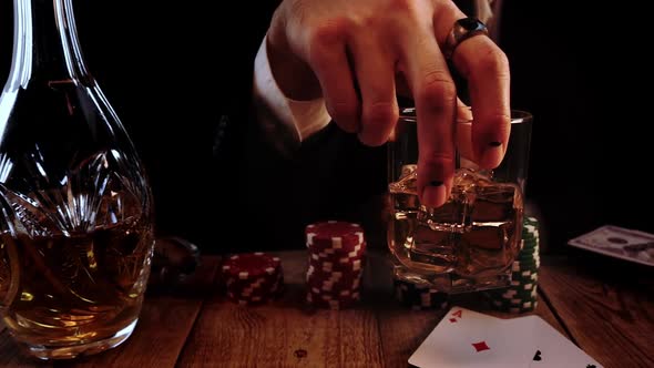 Closeup View of Man Holding a Glass Full of Whisky with Ice and Blending It During Poker in a Slowmo alt