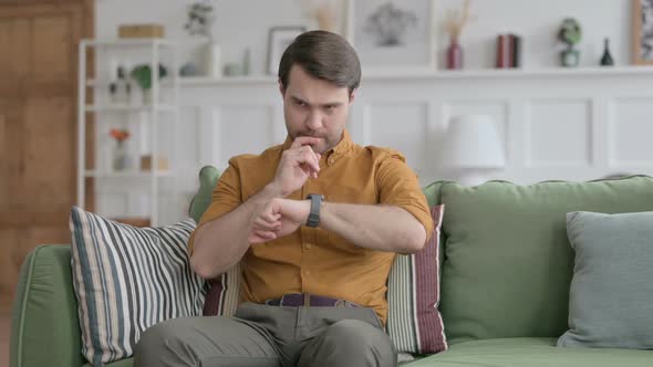 Young Man using Smart Watch while Sitting on Sofa alt