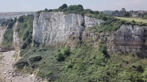 Rising aerial of cliffside beach with a small village in the horizon on a bright day. alt