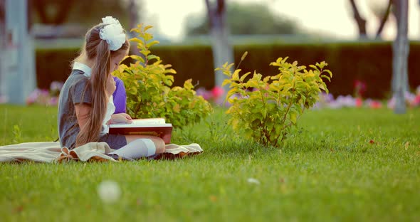 Young Pretty School Girl Reading Book in Park alt