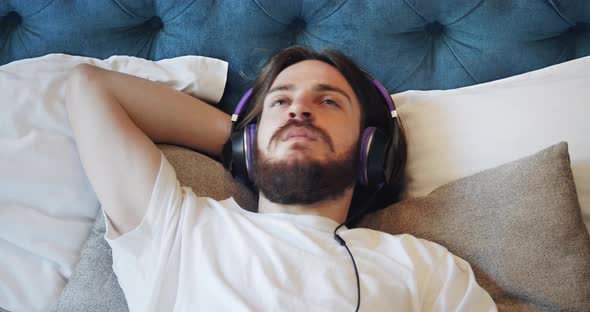 Male in Earphones Lying on Bed