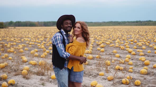 A Young Couple Stands Embracing in a Pumpkin Field alt