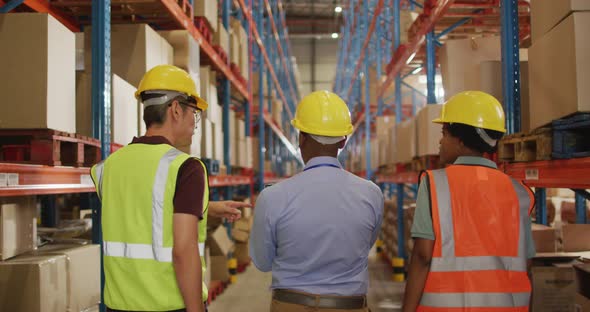 Diverse male and female workers wearing safety suits and talking in warehouse alt