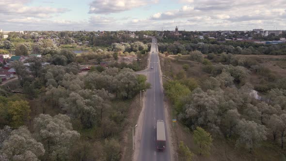 Fly Over a Small Road with Cars Green Trees and Cities in the Distance alt