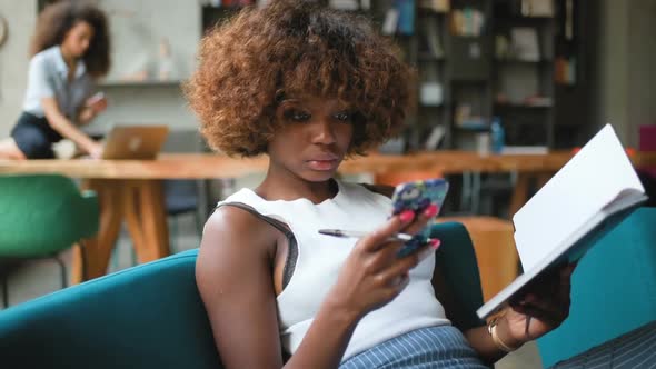 two young multiracial women writing and working with smartphone in modern coworking space alt
