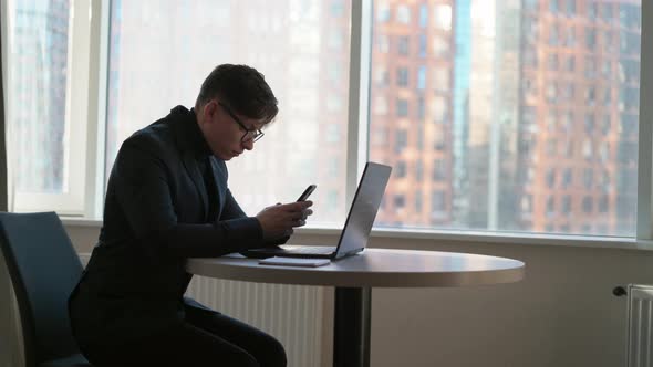 Smiling Young Businessman Holding Smartphone Sitting in Office Ceo 25 Years Old Wearing Glasses alt