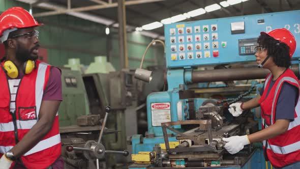 Factory worker helping colleague checking on industry machine alt