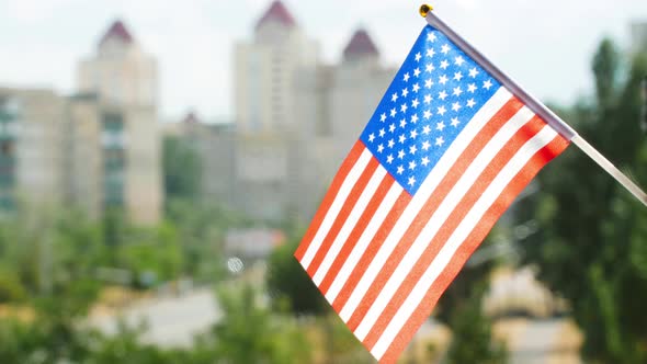 Flag of the United States of America set against blue sky, city street and buildings. Stars