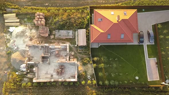 Top Down Aerial View of Two Private Houses One Under Construction with Wooden Roofing Frame and alt