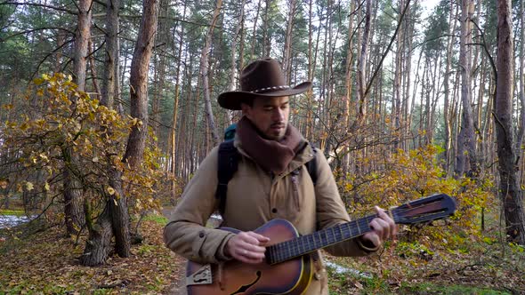 A Backpacker with a Guitar Walks Along a Trail in the Forest alt