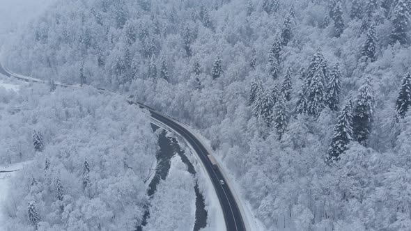 Aerial shot: cars and trucks are driving by the road in winter forest. alt