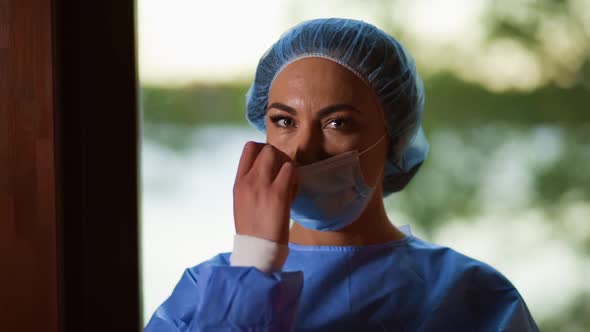 Close View of Young Female Doctor or Nurse Taking Off Surgical Face Mask and Looking at Camera alt