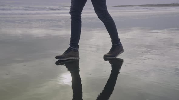 Man Hiking Over Wet Black Sand Beach alt