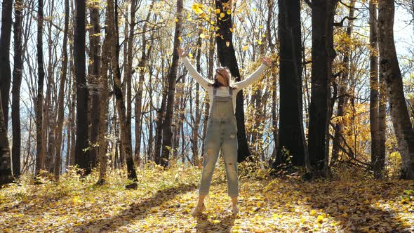 Happy Young Woman Having Fun and Throwing Yellow Leaves at Autumn Forest