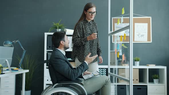 Young Woman and Disabled Man in Wheelchair Talking Writing on Sticky Notes on Glass Board in Office alt