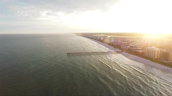 Drone flying over the ocean near a pier at sunset alt