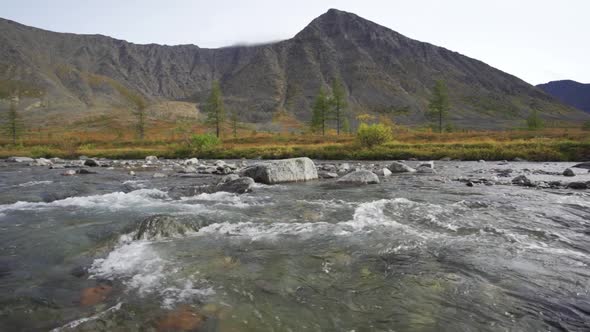 A Shallow River with a Rocky Bottom Flows Among High Mountains