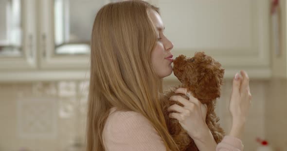 A poodle puppy licks the face of a young beautiful girl while she holds it in front of her face