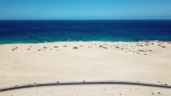 Above view of black asphalt road with desert and sand dunes around - coastline with blue ocean alt
