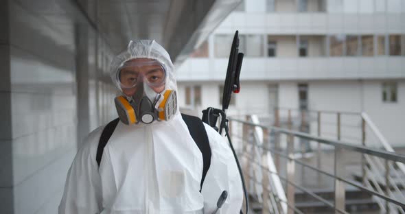 Worker Wearing Hazmat Suit Disinfecting Terrace in Office Building alt