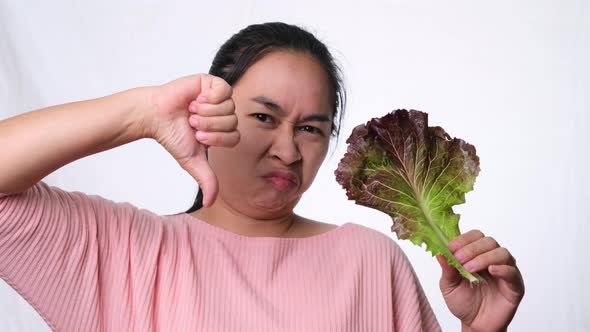 Asian woman hates fresh salad on white background in studio. alt