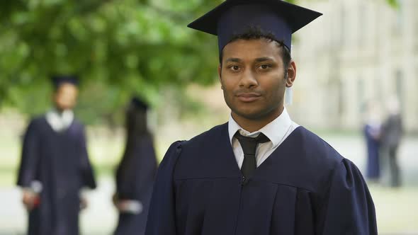 Guy in Graduation Outfit Crossing Arms with Diploma in Hand, Smiling Achievement alt