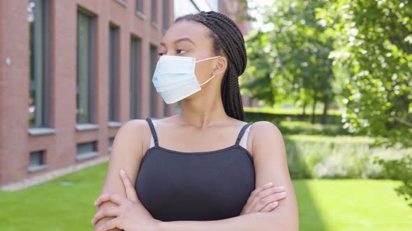 A Young Black Woman in a Face Mask Looks Around As She Waits for Someone - an Office Building alt