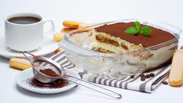 Traditional Italian Tiramisu dessert in glass baking dish, portion on plate and cup of coffee alt