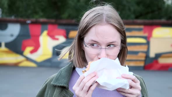 Delighted Young Woman with Short Hair Eats Burger in Cafe alt
