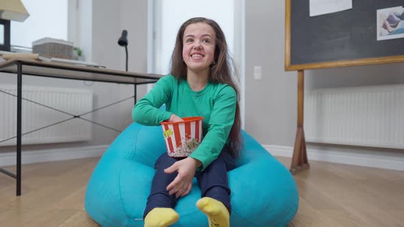 Laughing Carefree Woman Pointing Looking at Camera Watching TV at Home Indoors Eating Popcorn alt