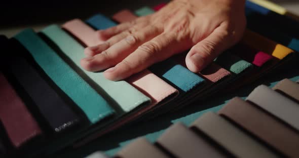 A Man's Hand Touches Samples of Multicolored Fabric alt