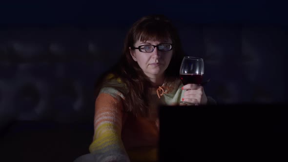 Brunette Woman Watches Tv in the Evening at Home with a Glass of Wine Moving Camera