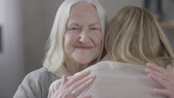 Portrait of Happy Old Caucasian Mother Hugging Daughter at Home Indoors Looking at Camera alt