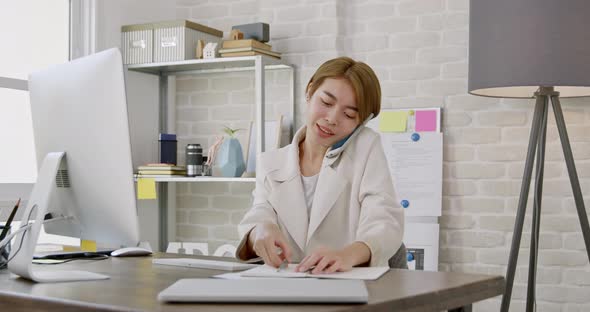 Young Asian woman entrepreneur talking on mobile phone while working in home office