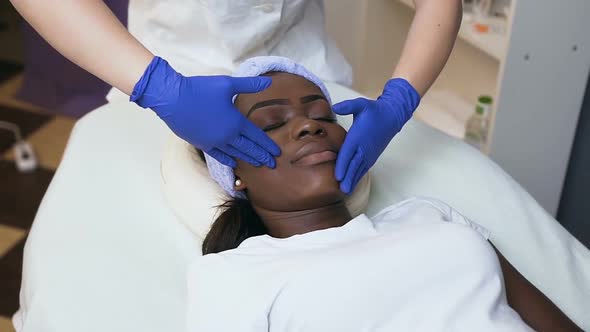 Female Cosmetologist Hands Making Massage for Attractive African Woman alt